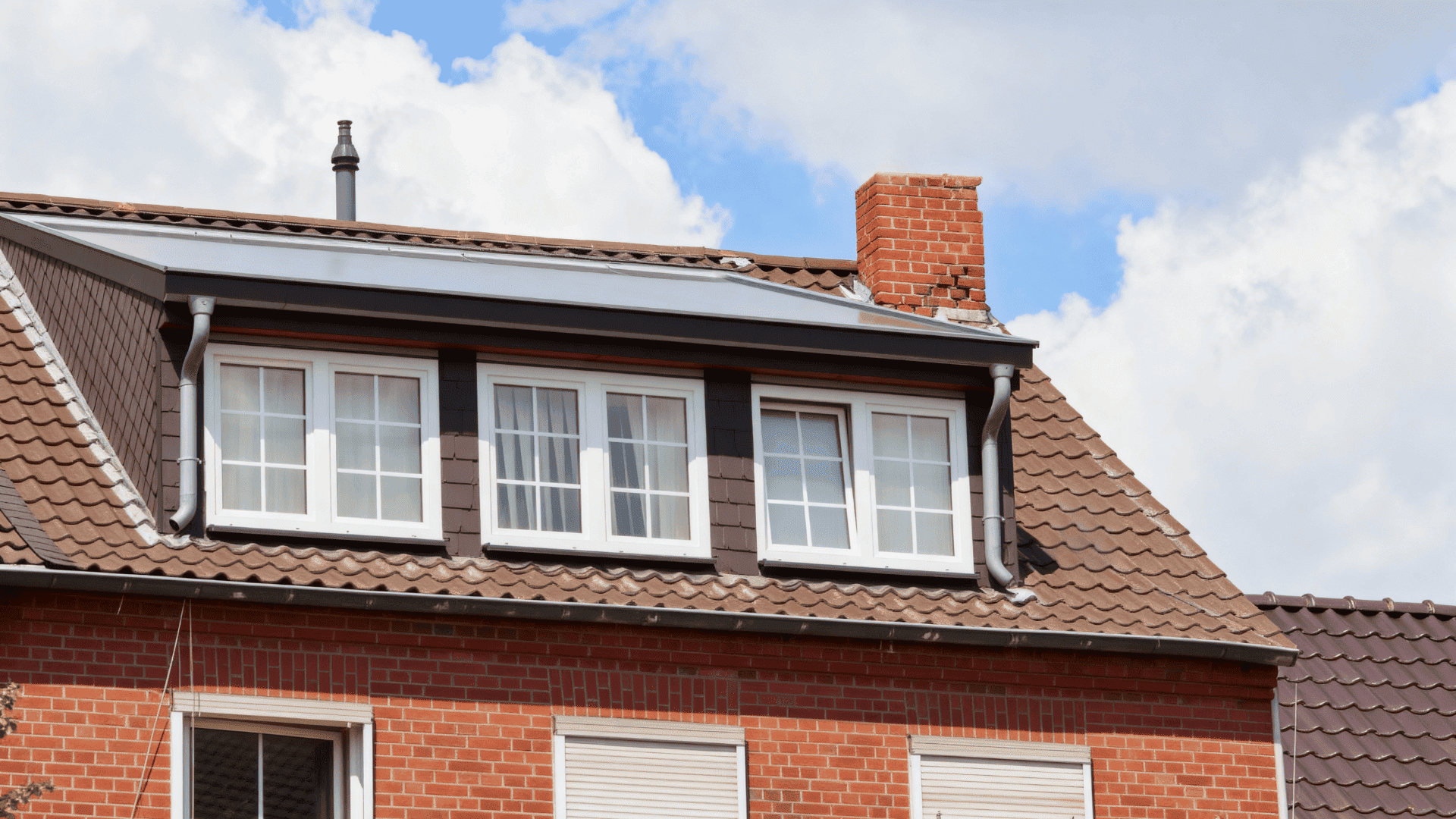 Large wall dormer with multiple windows on a tiled brick house roof