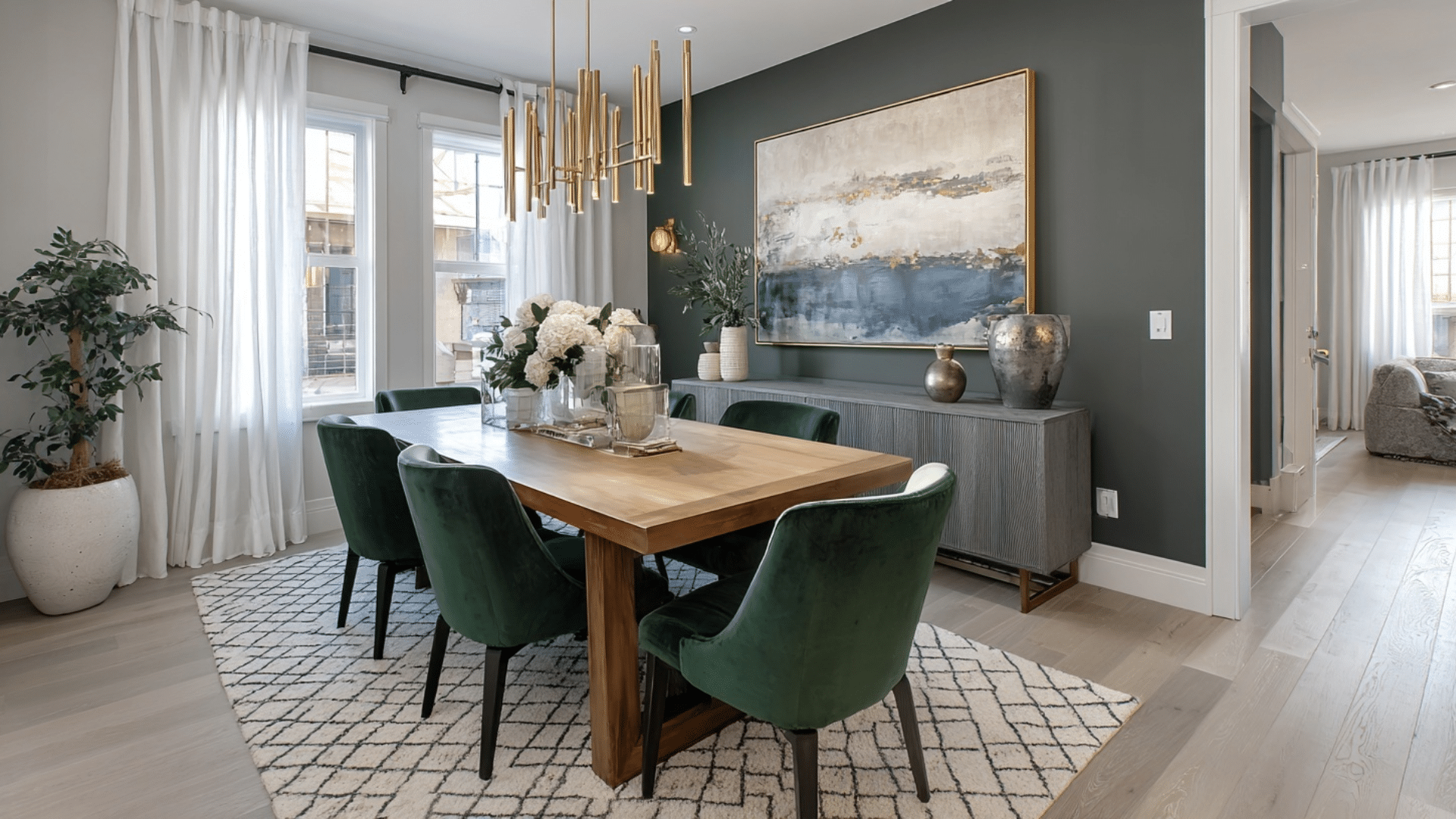 Modern dining room with a wood table green velvet chairs a gold chandelier gray accent wall and white patterned area rug