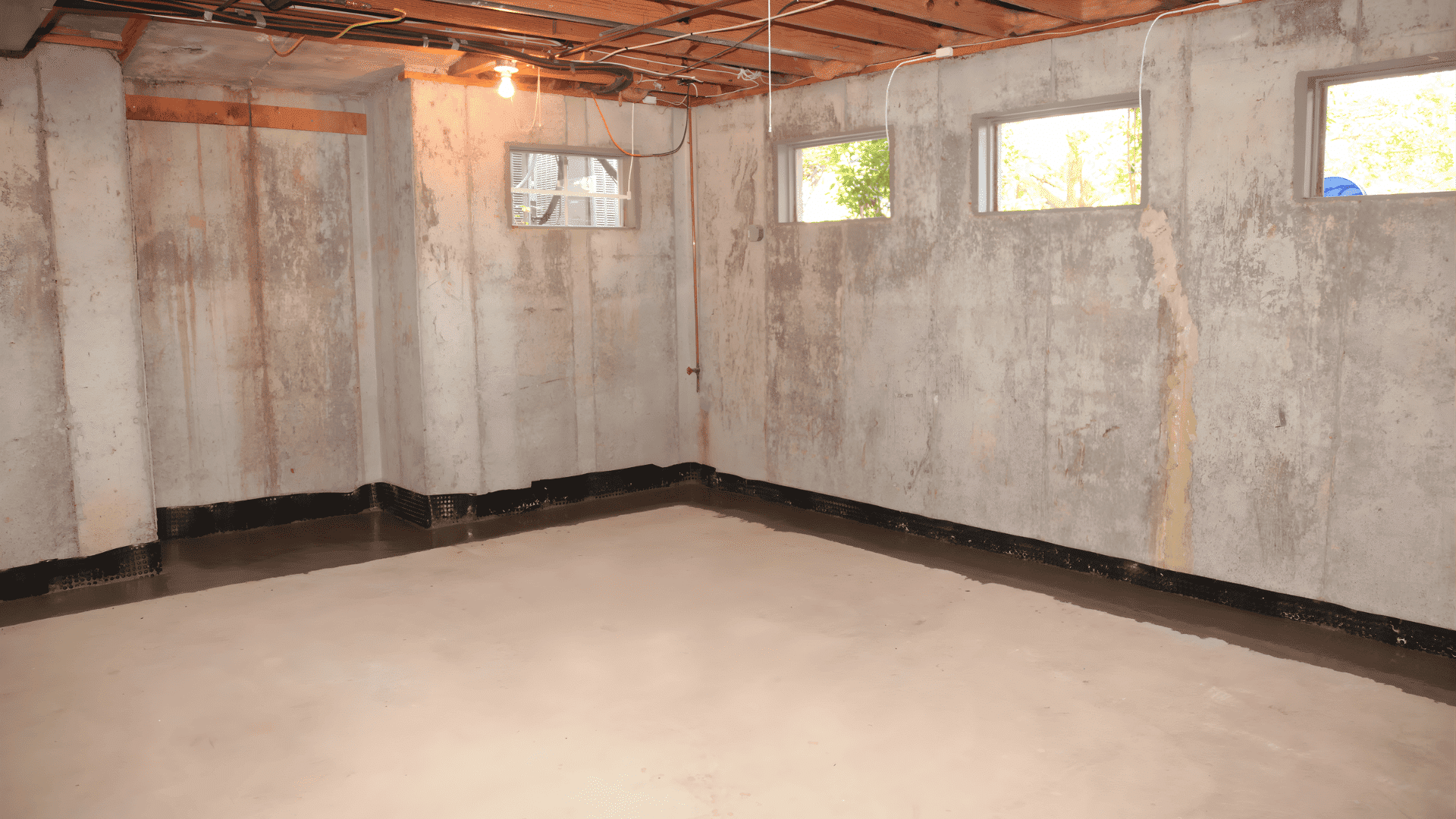 A basement room featuring bare concrete walls and floor, highlighting waterproofing measures for moisture control.