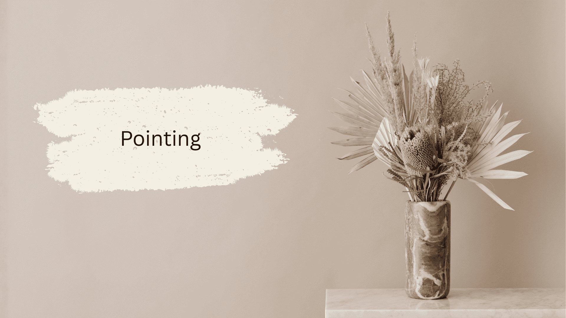 A decorative arrangement of dried flowers in a textured vase on a light-colored surface, next to the word Pointing on a neutral background