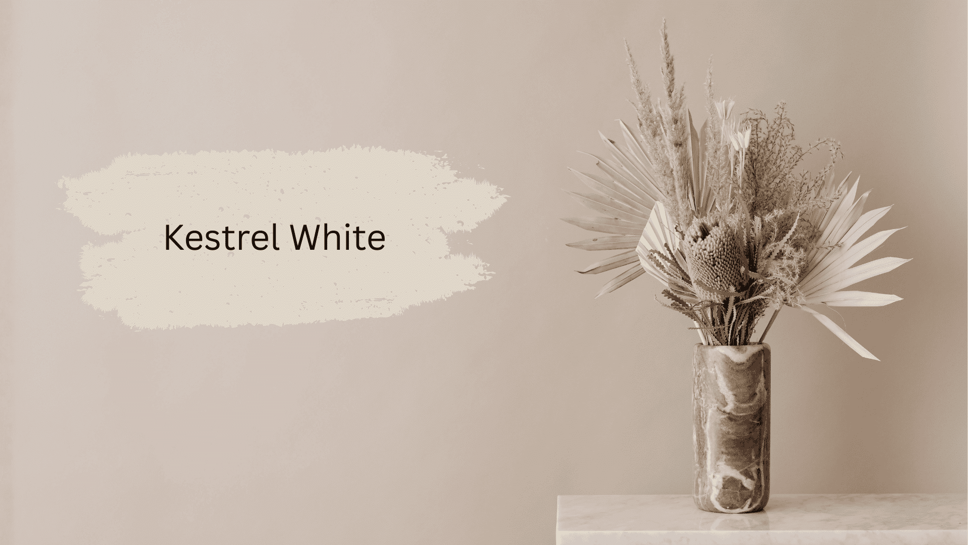 A paint swatch of Kestrel White is displayed on a neutral beige wall next to a marbled vase holding a bouquet of dried natural grasses and palms