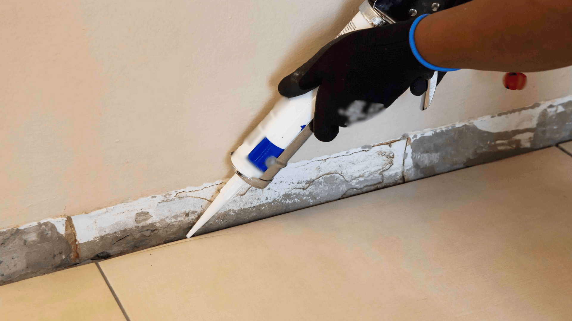 A person applying caulk with a gun to repair a floor as part of an interior waterproofing project