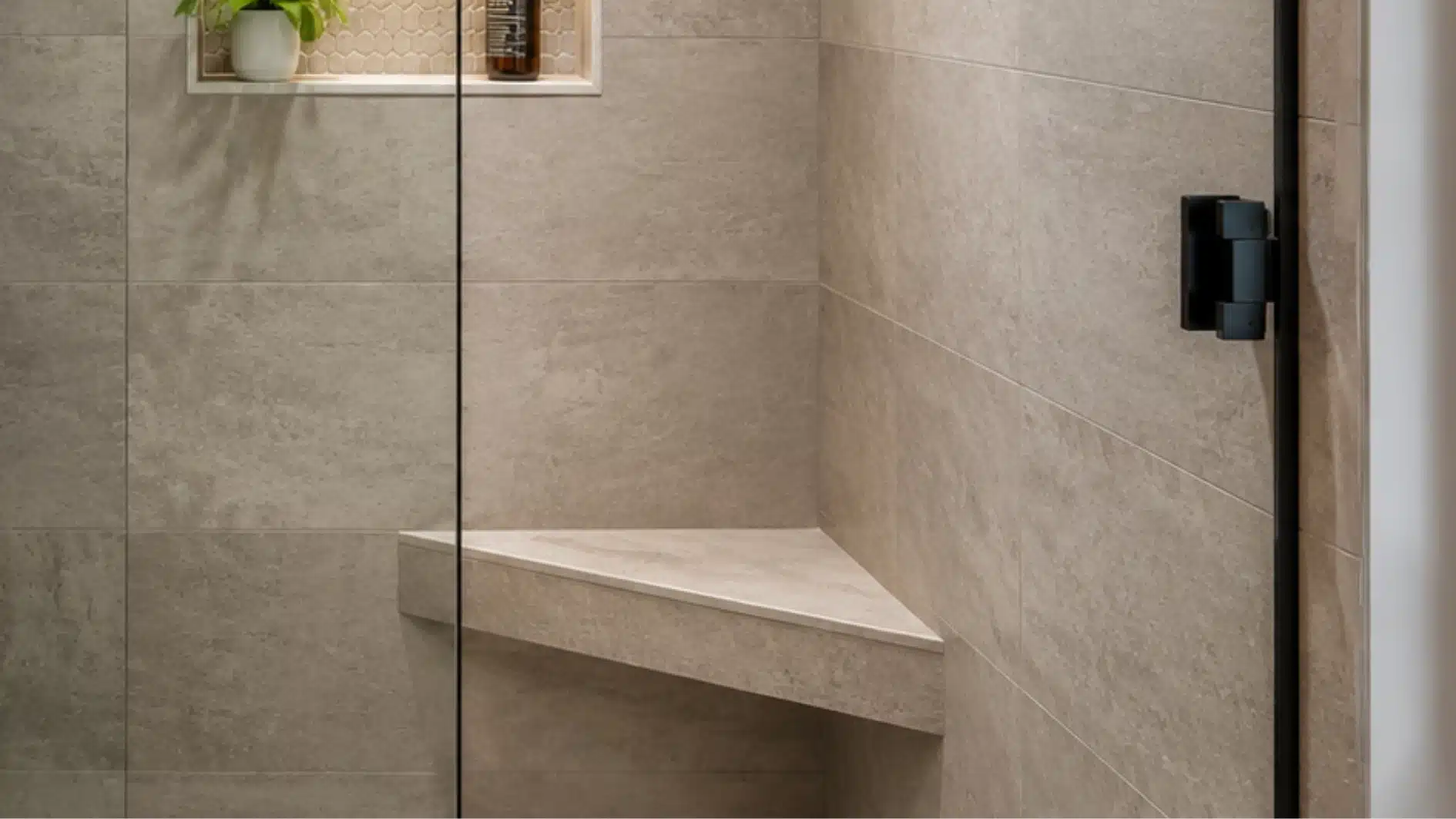 Modern walk-in shower featuring beige tiled walls, a built-in corner bench, and a frameless glass door with black hardware.