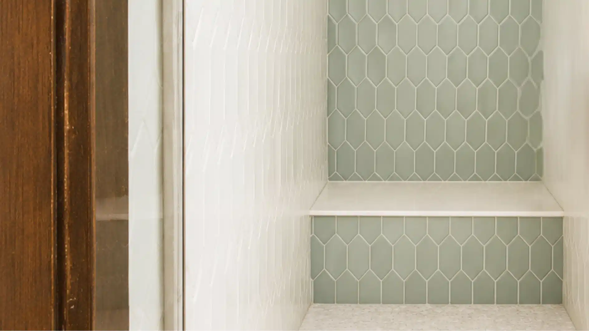 Close-up of a modern shower niche featuring light sage green elongated hexagonal tiles on the back wall and white elongated subway tiles on the side wall, with a white built-in shelf.