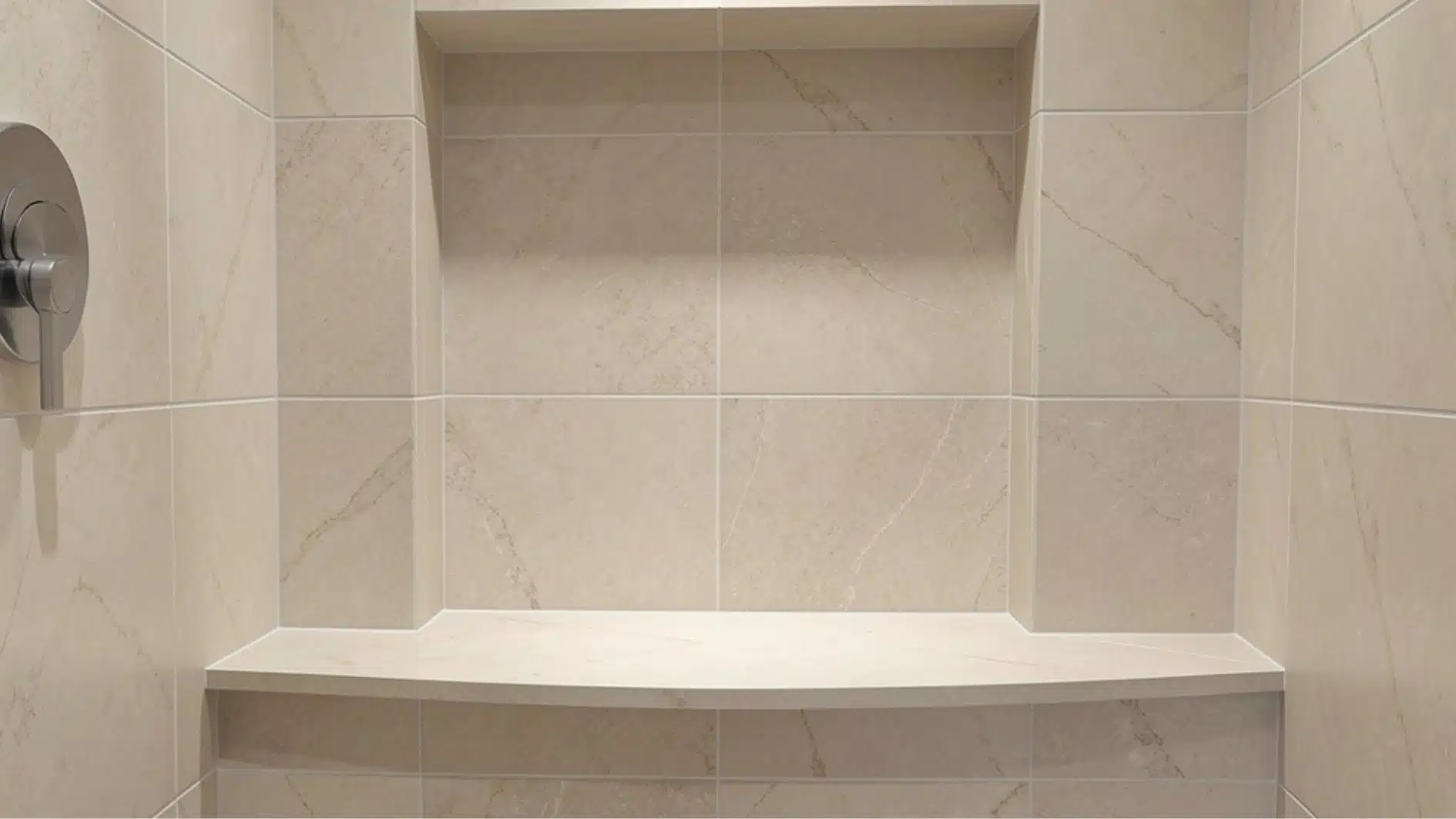 Beige tiled shower interior featuring a built-in curved bench seat and a recessed wall niche, with a brushed metal shower handle visible on the left.