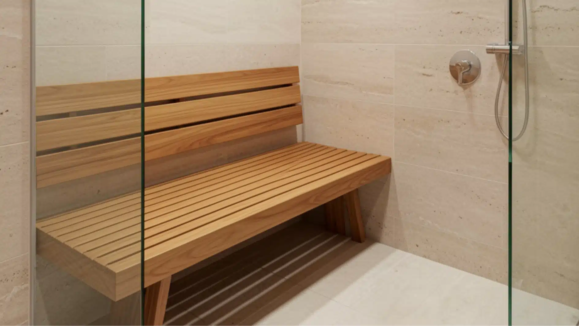 Wooden slatted shower bench inside a walk-in shower with beige tiled walls and a glass partition.